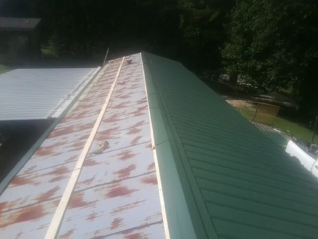 Old rusted panels beside newly installed green metal roofing — Wind Damage Roof Repair by Roofing Brothers in Norwich